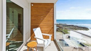 A balcony with a view of the beach, a white chair, and a small wooden table. - Seaside Tranquility|North Pier Ocean Villa+Pool| (Carolina Beach)