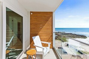 Ein Balkon mit Blick auf den Strand, ein weißer Stuhl und ein kleiner Holztisch.