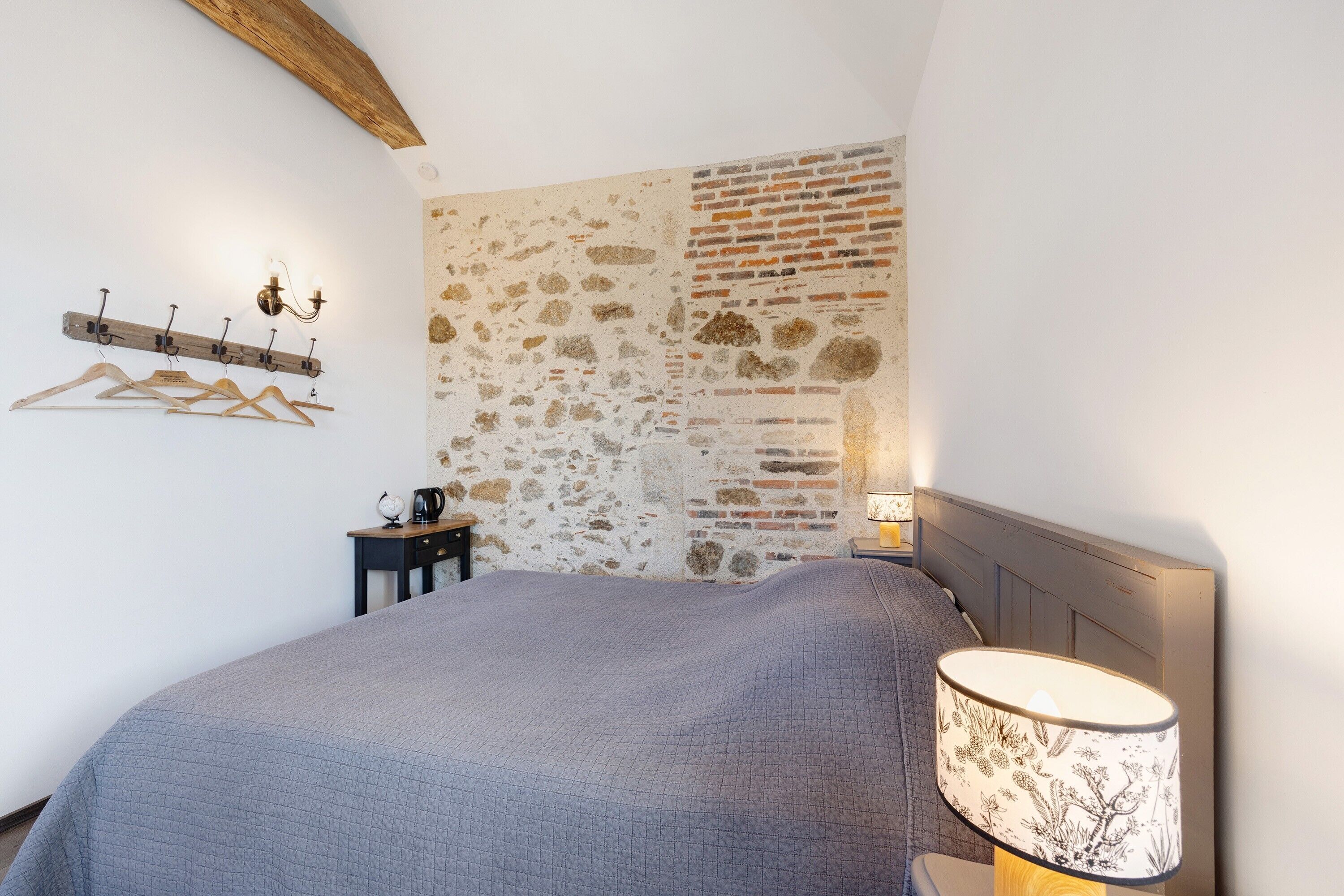 Ein Schlafzimmer mit einem Bett, einem Wandhaken für Kleidung, einer Lampe und einem kleinen Tisch mit Globus und Wasserkocher.