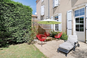 Eine Terrasse mit Gartenmöbeln, einem grünen Sonnenschirm und einer Hecke.
