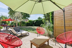 Ein Patio mit einem Tisch, zwei roten Stühlen, einem roten Sonnenschirm und einem Holzzaun.