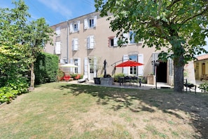 A courtyard with a lawn, a red umbrella, outdoor furniture, and a building with multiple windows and balconies.