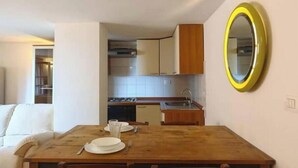 Una cocina compacta con armarios blancos, una mesa de madera para dos personas y un espejo con marco amarillo en la pared.