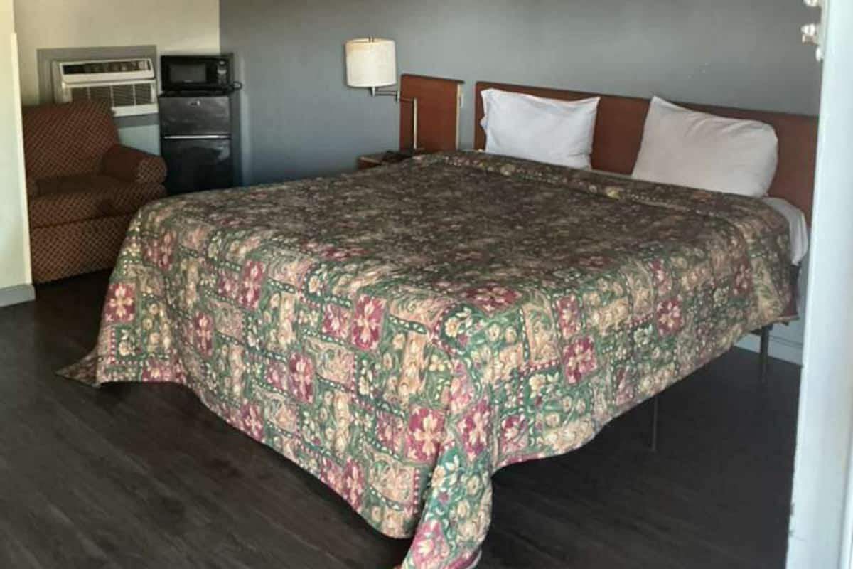 A hotel room with a bed, a desk, a chair, and a microwave.