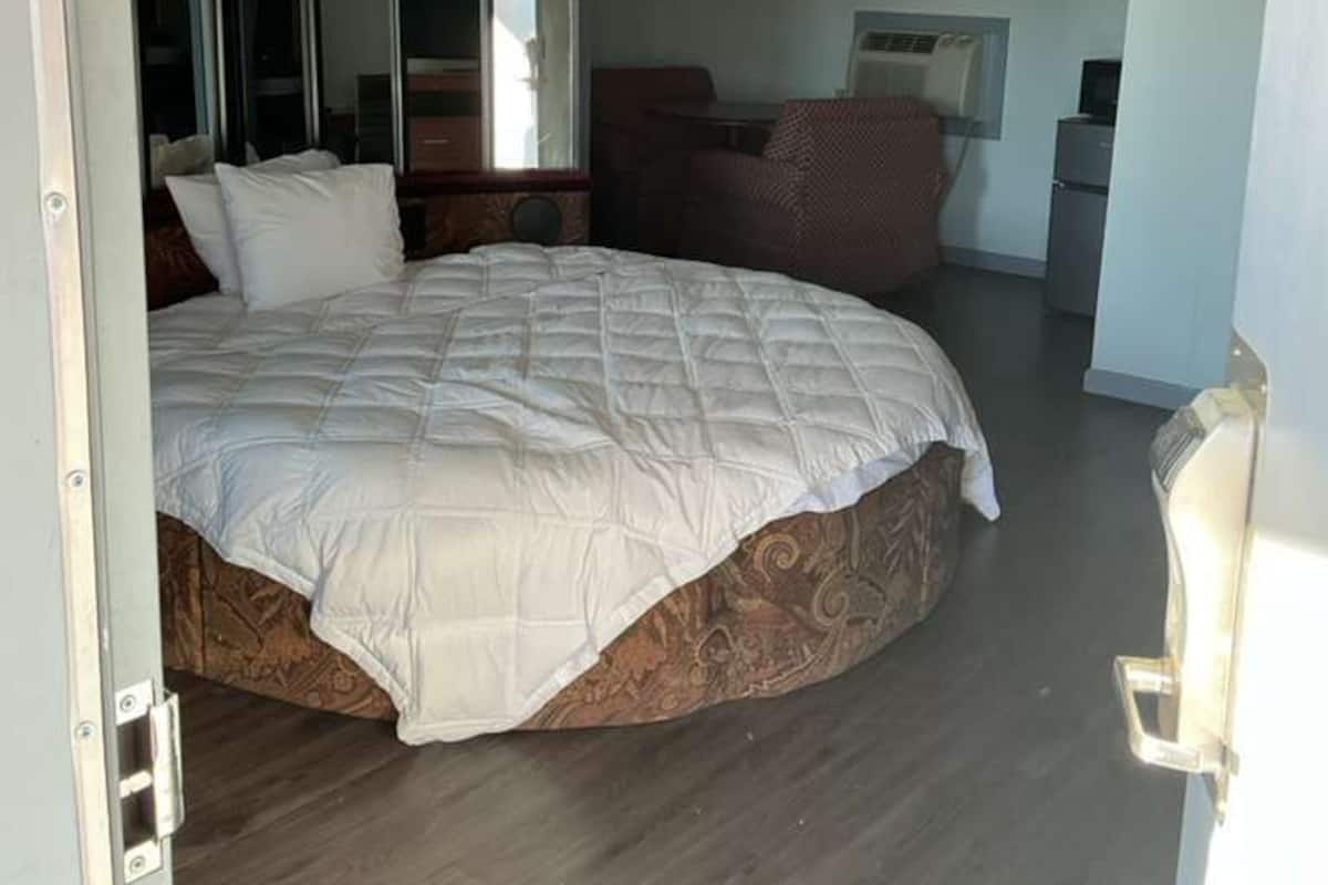 A bedroom with a large bed, a wardrobe with mirrors, a desk, and a chair.