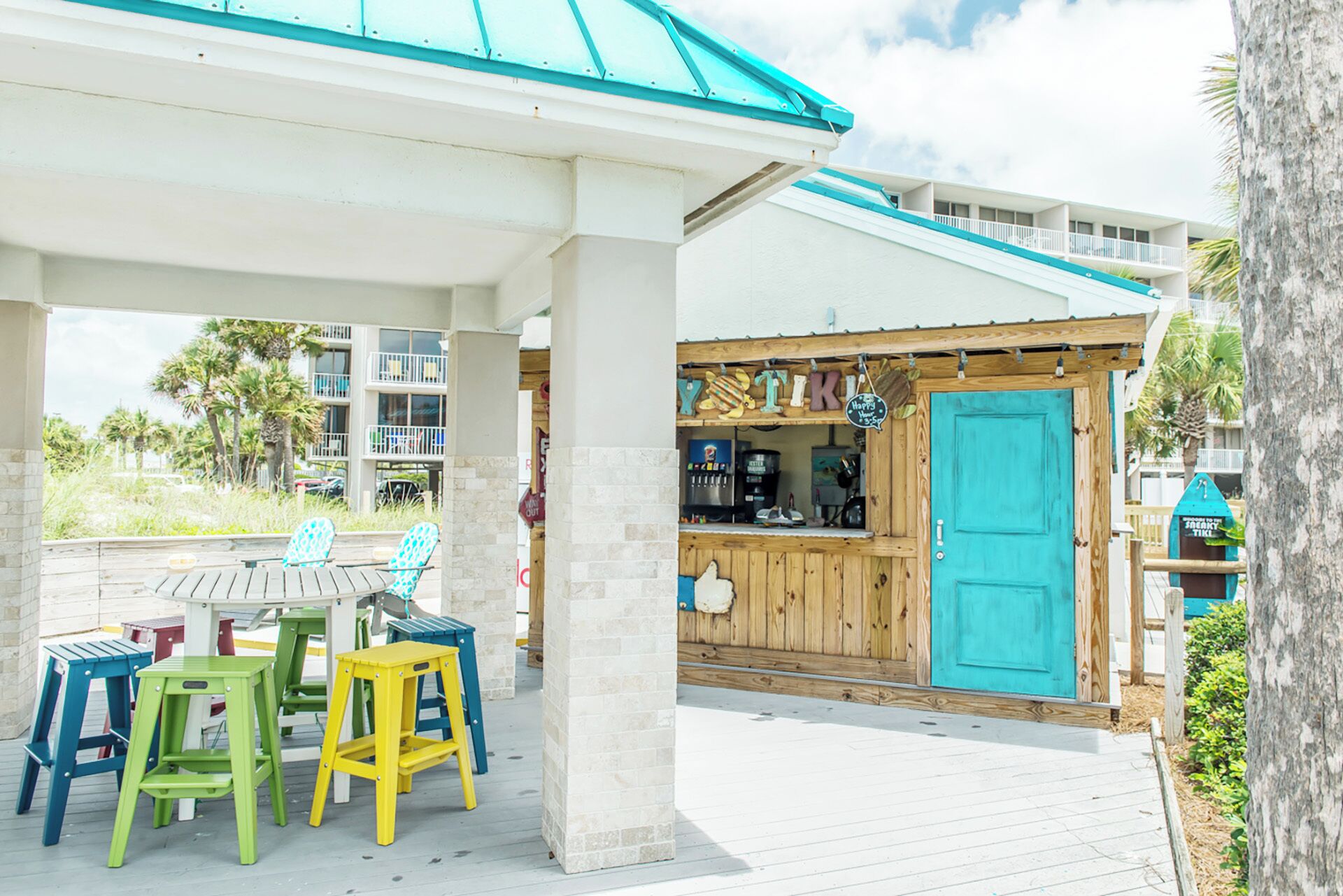 A covered outdoor seating area with colorful chairs and a wooden bar with a turquoise door.
