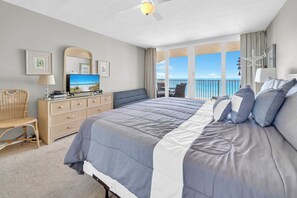 Quarto com cama, cômoda, cadeira, televisão e varanda com vista para o mar.