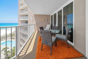 Uma varanda com vista para a praia, uma piscina e uma área de refeições com cadeiras e mesa de vime.
