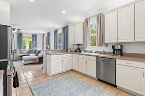 Eine moderne Küche mit weißen Schränken, einem Geschirrspüler, einer Kaffeemaschine und einem Essbereich mit Sofa und Tisch.