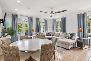 Ein modernes Wohnzimmer mit einem runden Esstisch, Korbstühlen, einer Couch und einem Deckenventilator.