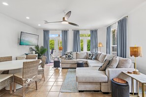 Ein modernes Wohnzimmer mit einer Couch, einem Esstisch, Stühlen und einem Deckenventilator.