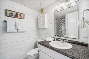 Ein Badezimmer mit einer weißen Toilette, einem Waschbecken mit Granitplatte, einem großen Spiegel und einem Handtuchhalter.