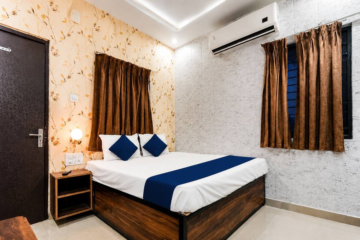 Un dormitorio con cama, mesita de noche, aire acondicionado y una ventana con cortinas.