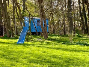 A playground with a slide and swings, surrounded by trees.