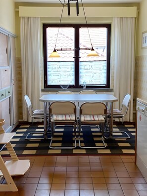 Un comedor con una mesa y cuatro sillas, una ventana con cortinas y un piso de baldosas.
