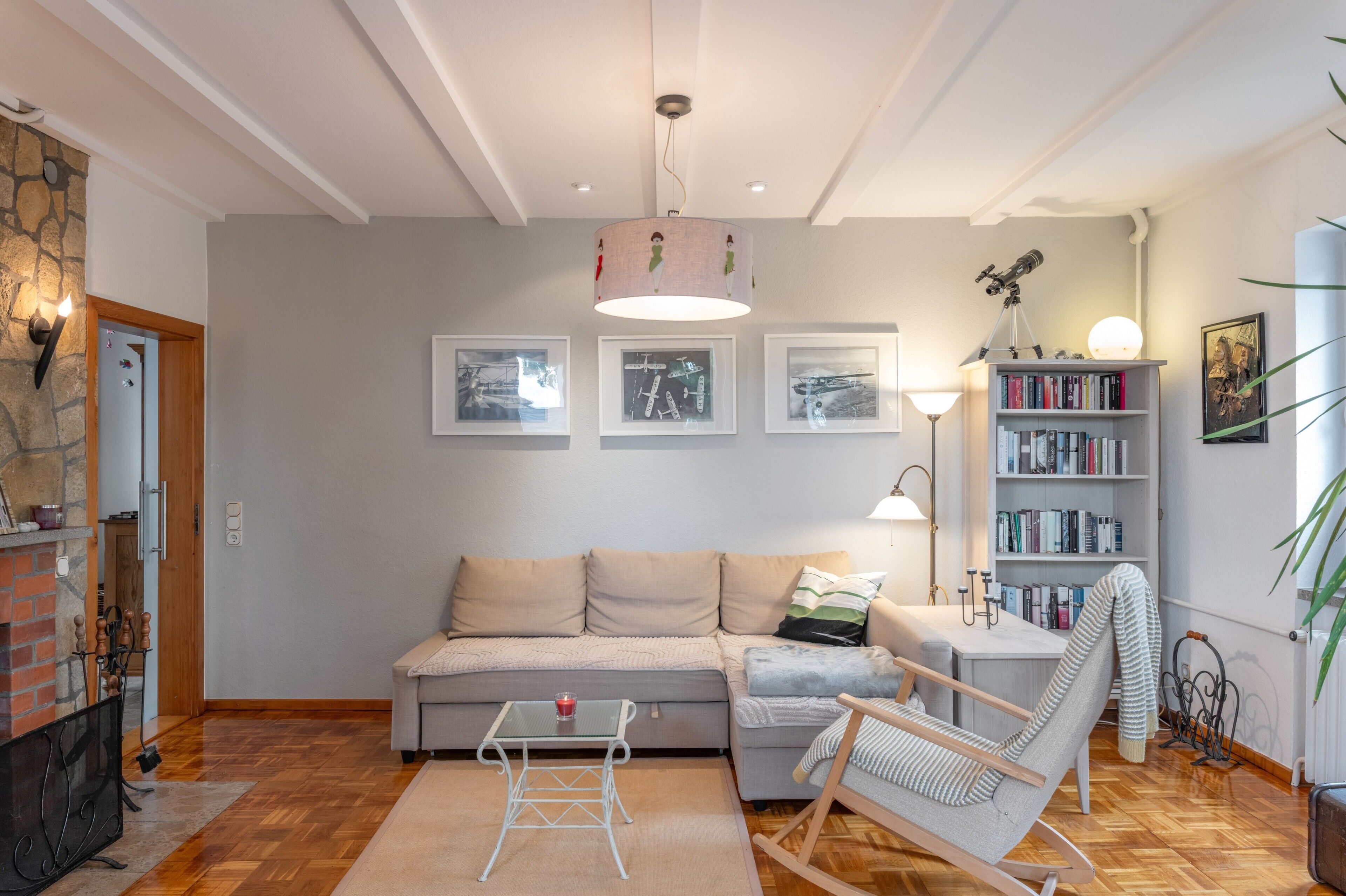 A living room with a sofa, a small table with a candle, a bookshelf, and a telescope.
