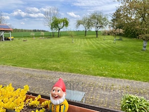 Ein Garten mit einer Gartenzwerg-Figur, einem Metallstuhl und einem grünen Rasen.