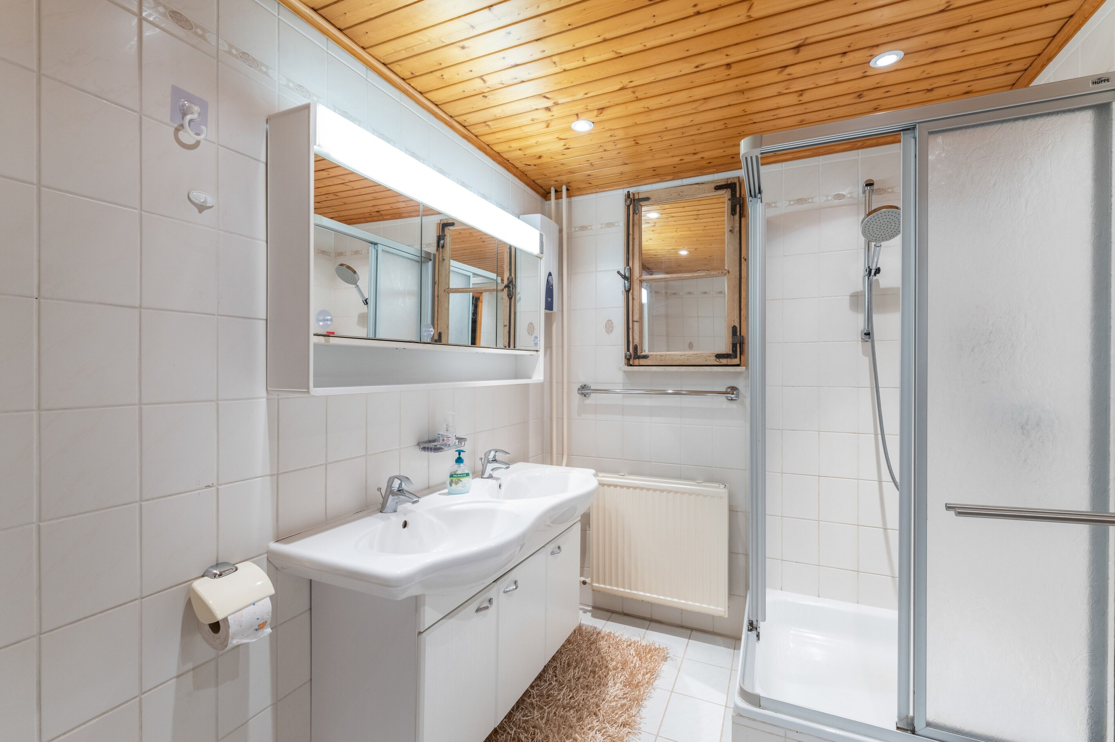 Ein modernes Badezimmer mit Holzbalkendecke, einer Duschkabine aus Glas und einer Wand mit weißen Fliesen.