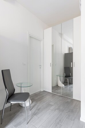 Ein modernes Zimmer mit Glastisch, einem Sessel und einem Spiegelkleiderschrank.