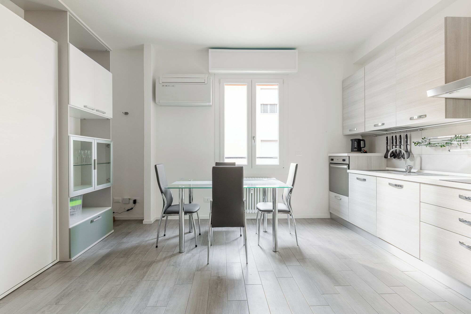 Ett modernt kök med vita skåp, ett matbord med stolar och ett fönster som släpper in naturligt ljus.