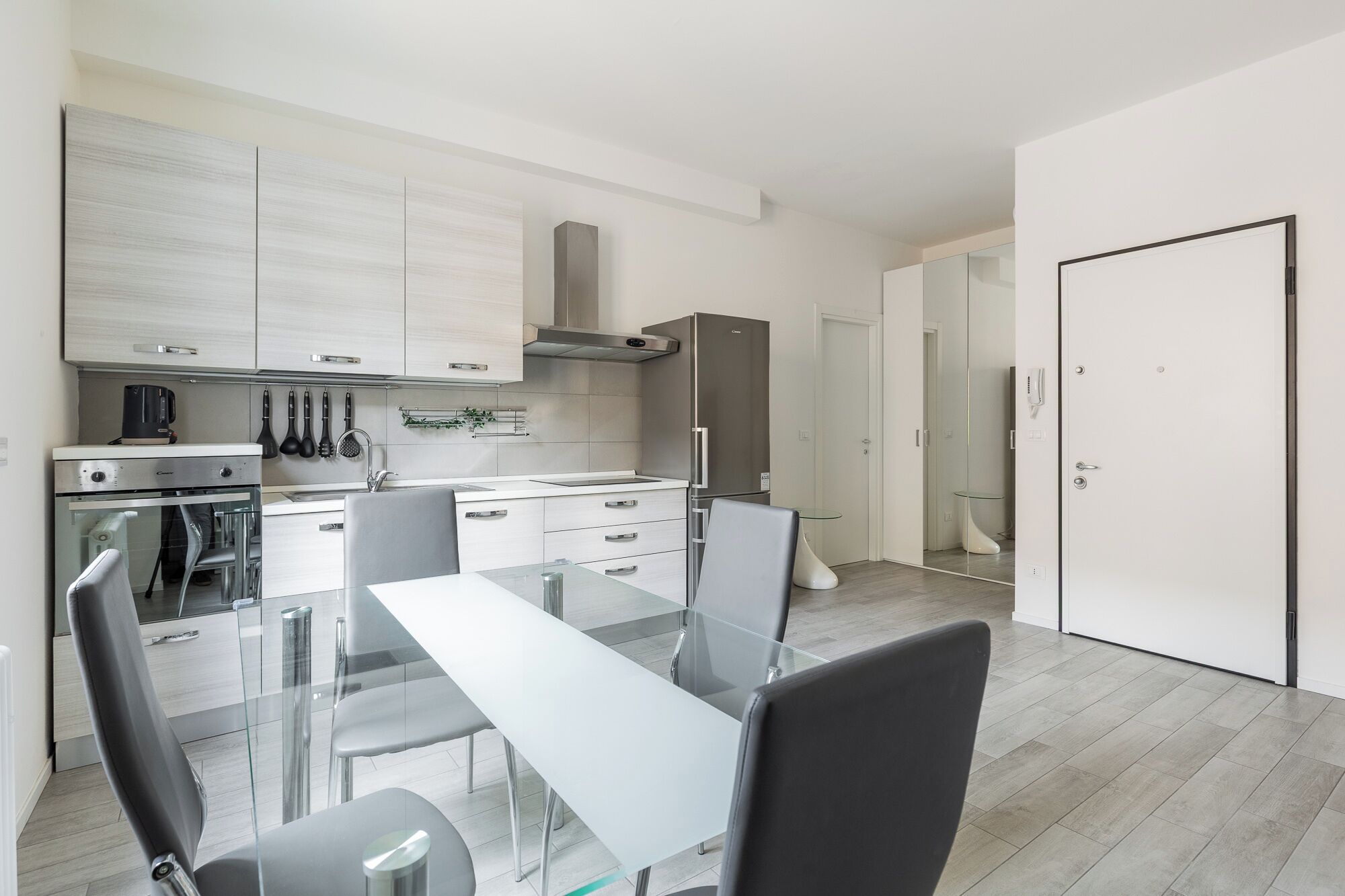 A modern kitchen with a dining area, stainless steel appliances, and a glass table.