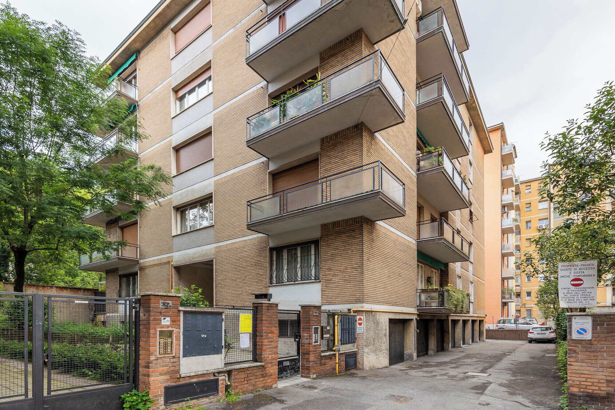 A multi-story residential building with balconies, a gated entrance, and a parking area.