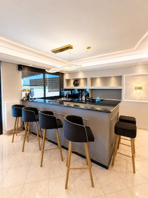 A modern kitchen with a bar area, featuring a central island, bar stools, and built-in appliances.