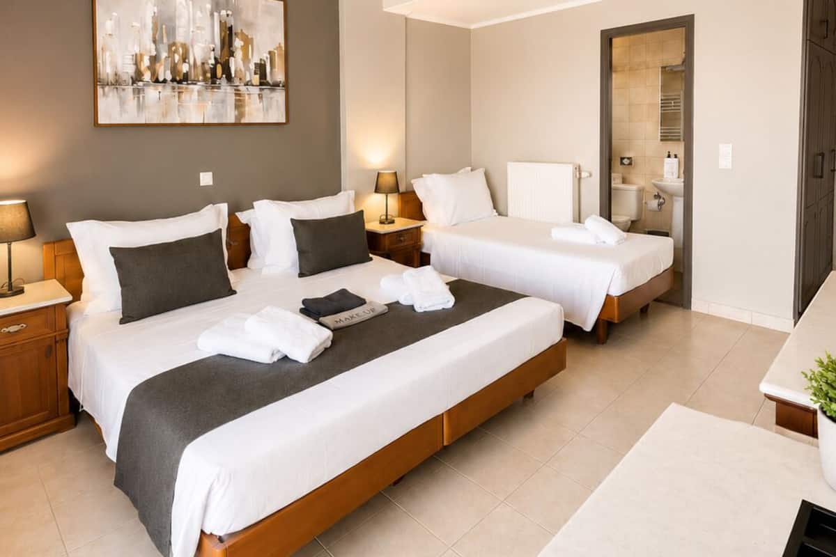 A modern hotel room with two beds, a large abstract painting, a desk, and a bathroom visible through an open door.