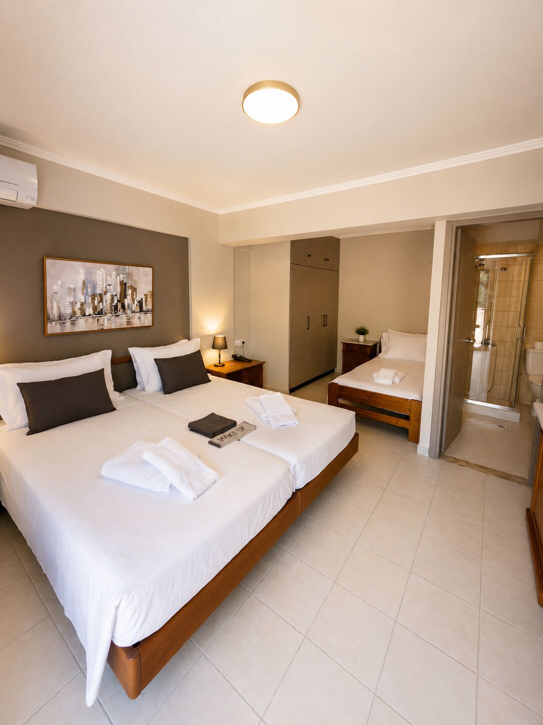 A hotel room with a large bed, a bedside table with a lamp, a wardrobe, and a shower area.