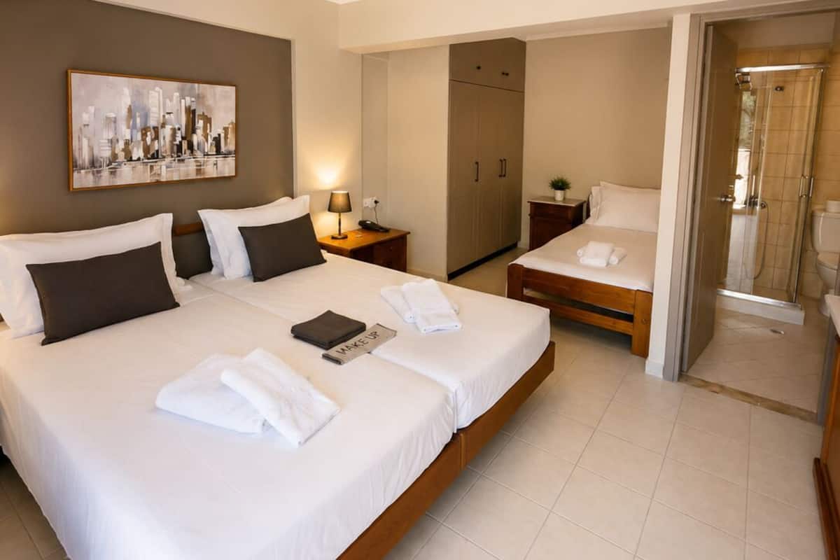 A hotel room with a large bed, a bedside table with a lamp, a wardrobe, and a shower area.