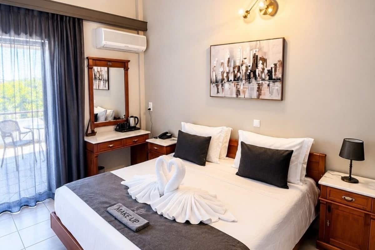 A hotel room with a large bed, a desk, a chair, a mirror, a painting, and a window with curtains.