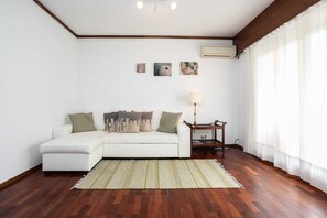 Una sala de estar con un sofá blanco, una mesita, una lámpara y tres obras de arte en la pared.