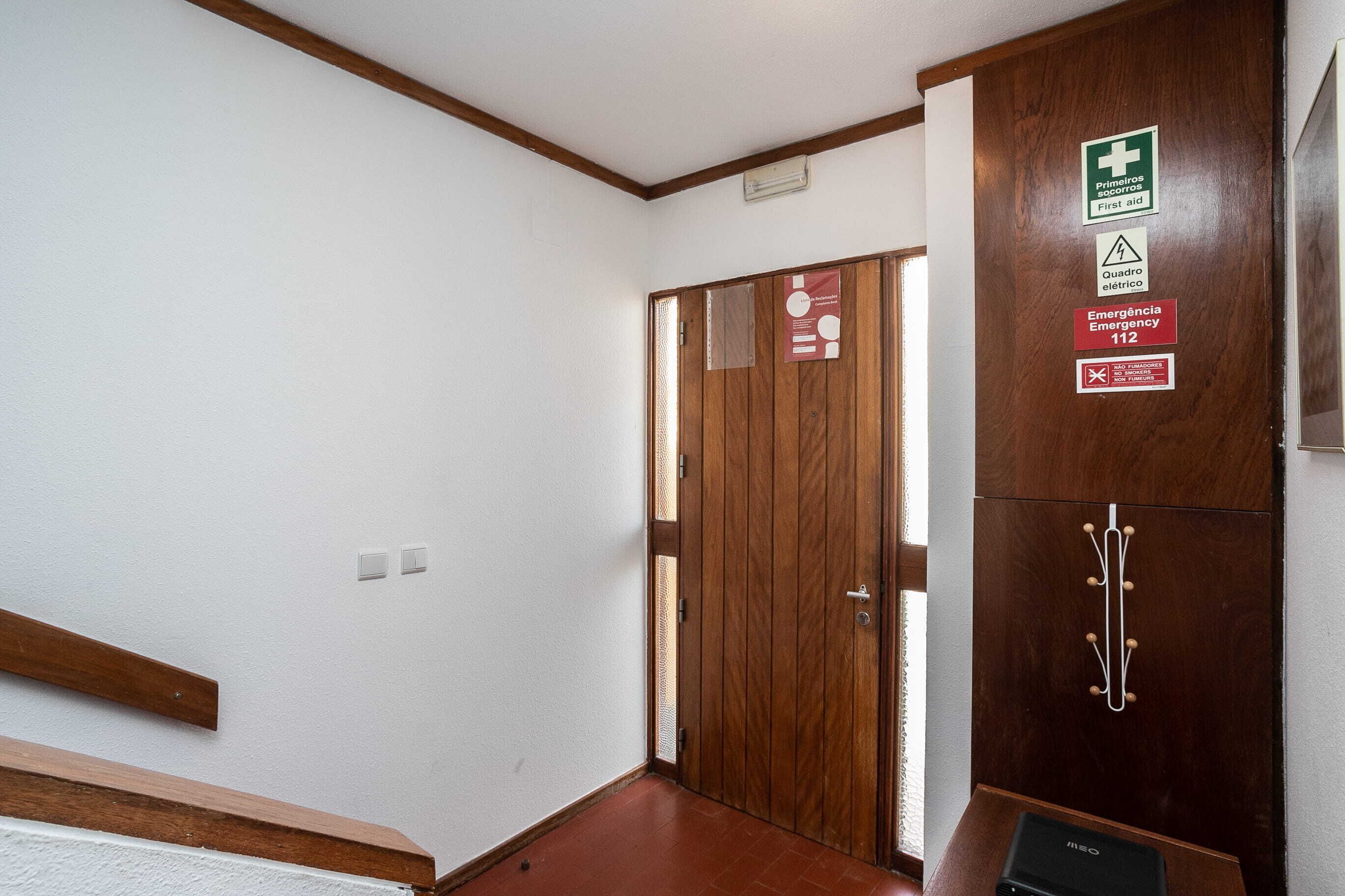 Un couloir avec une porte en bois, des panneaux d’indication pour les issues de secours et un porte-manteau.