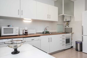 Una cocina moderna con armarios blancos, microondas, tostadora, lavamanos y un cubo de basura.