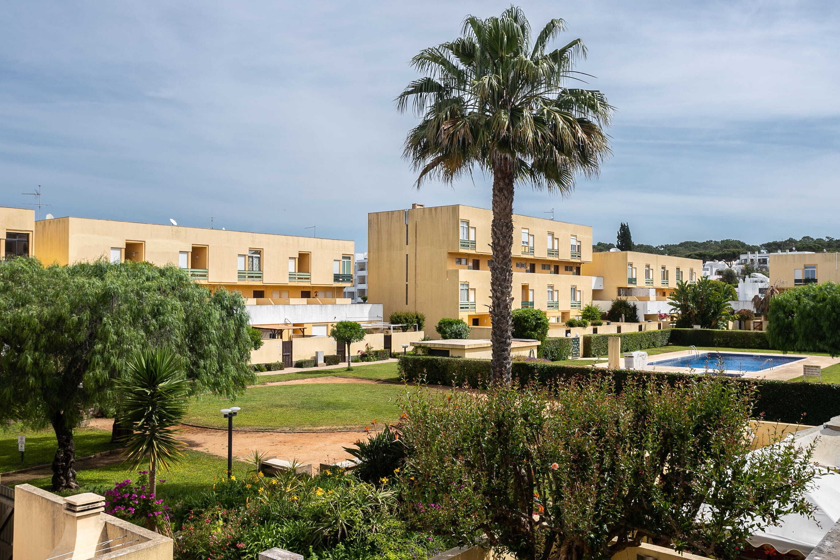 A residential building complex with multiple apartment buildings, a palm tree, and a swimming pool.