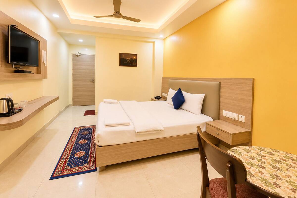 A hotel room with a bed, bedside table, chair, TV, and a ceiling fan.