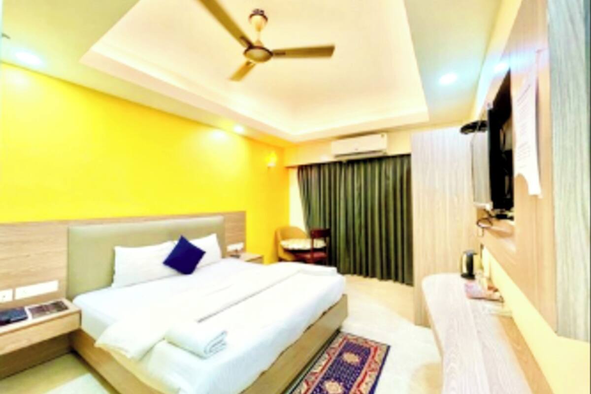 A hotel room with a bed, a ceiling fan, a TV, a desk, and a window with curtains.
