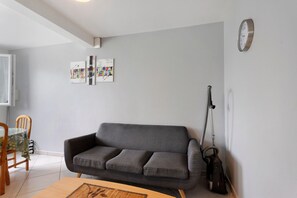 Ein Wohnzimmer mit grauem Sofa, einem Esstisch und einem Staubsauger.