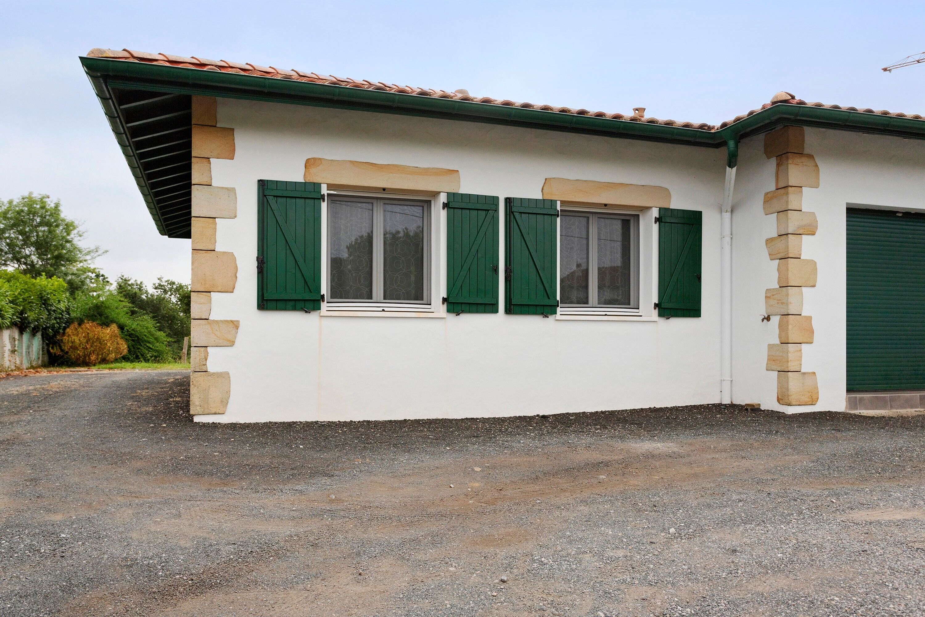 A building with two windows, a garage door, and a gravel driveway.