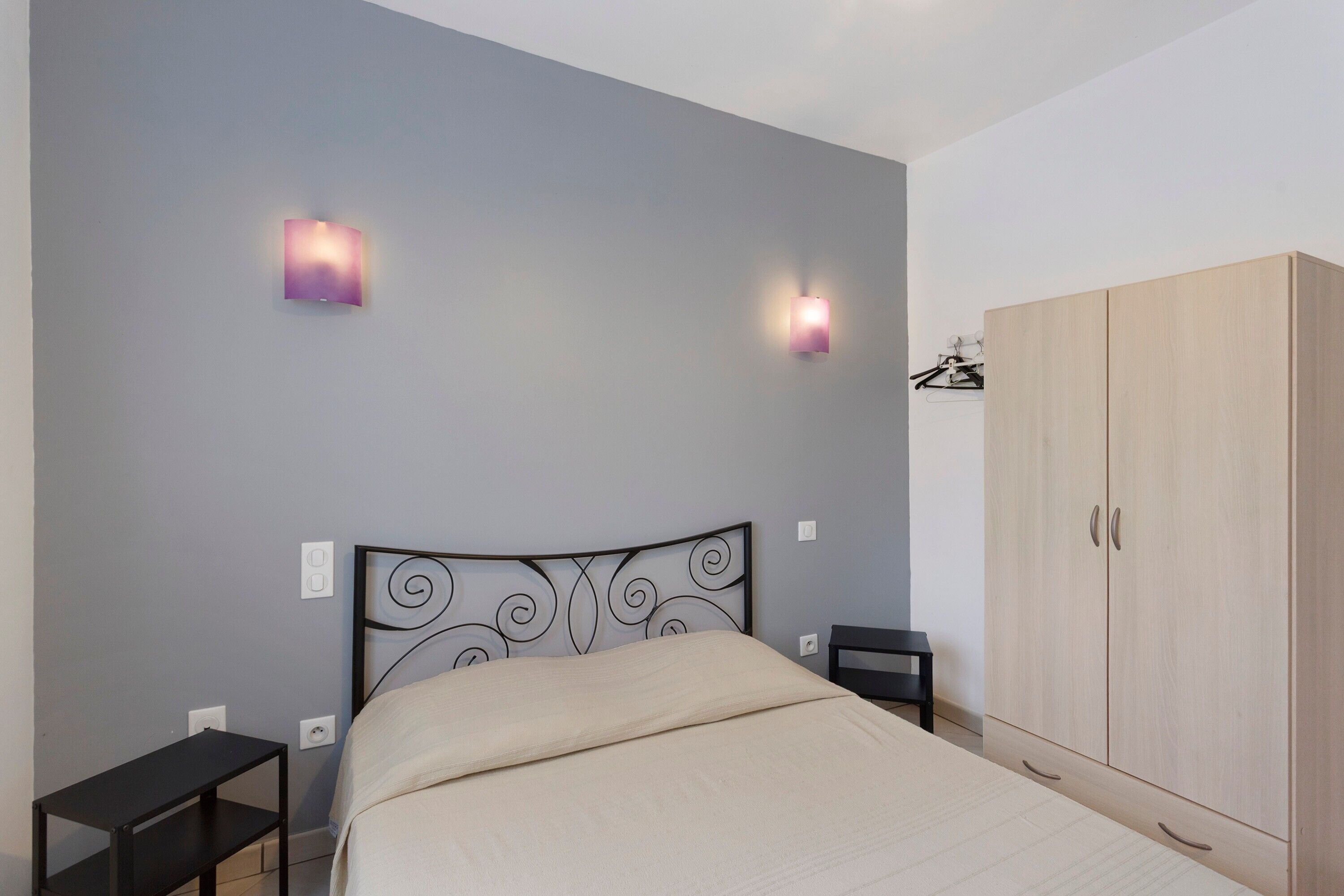 A bedroom with a bed, two wall-mounted lights, a wardrobe, and a bedside table.