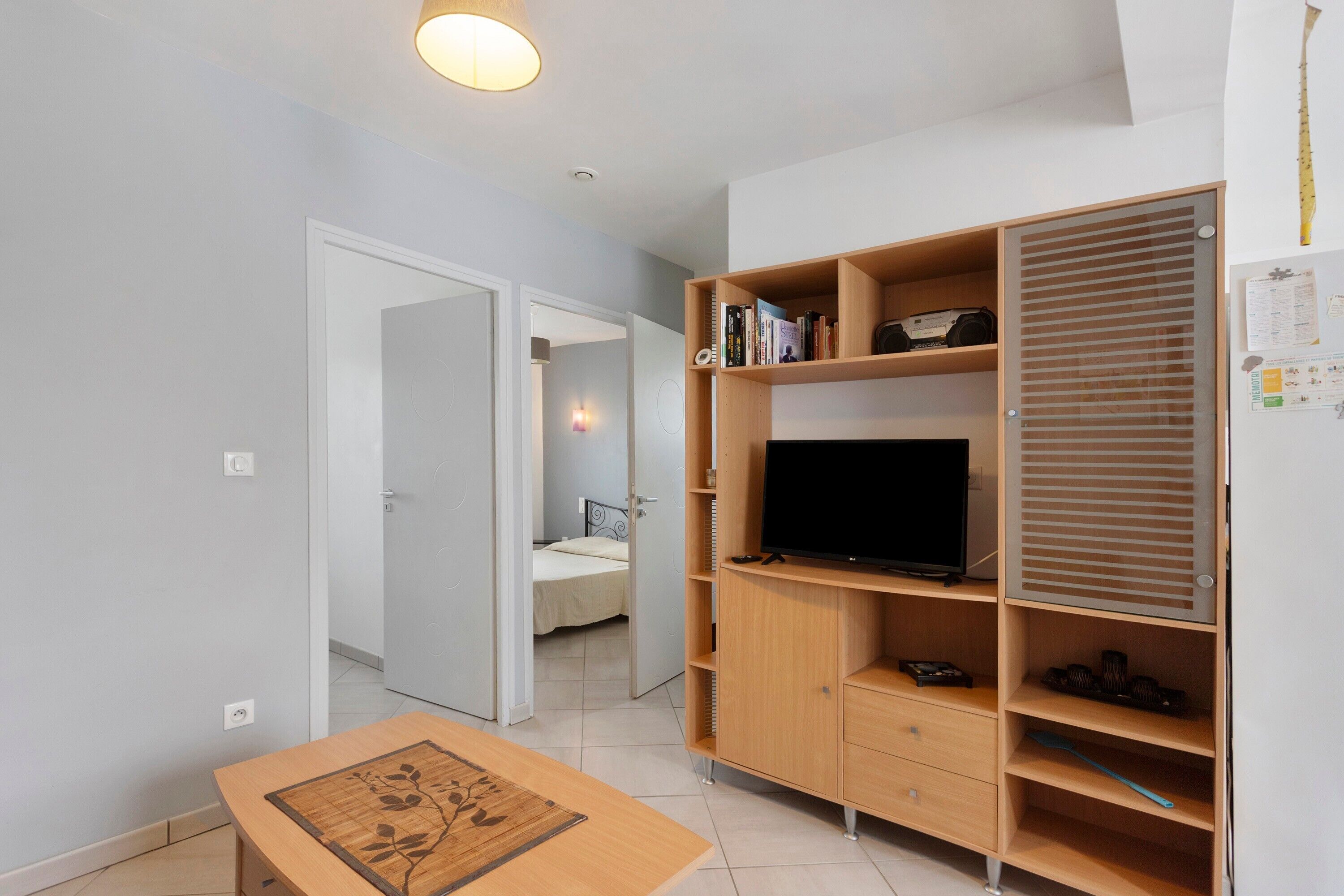 A room with a wooden TV stand, a small table, and a bed in the background.