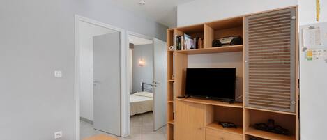 A room with a wooden TV stand, a small table, and a bed in the background.
