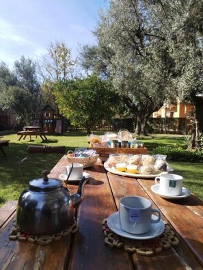 An outdoor dining table with a teapot, cups, and food items, surrounded by trees and a building in the background. - CABAÑAS CALDERON COMPLEJO I (San Rafael)