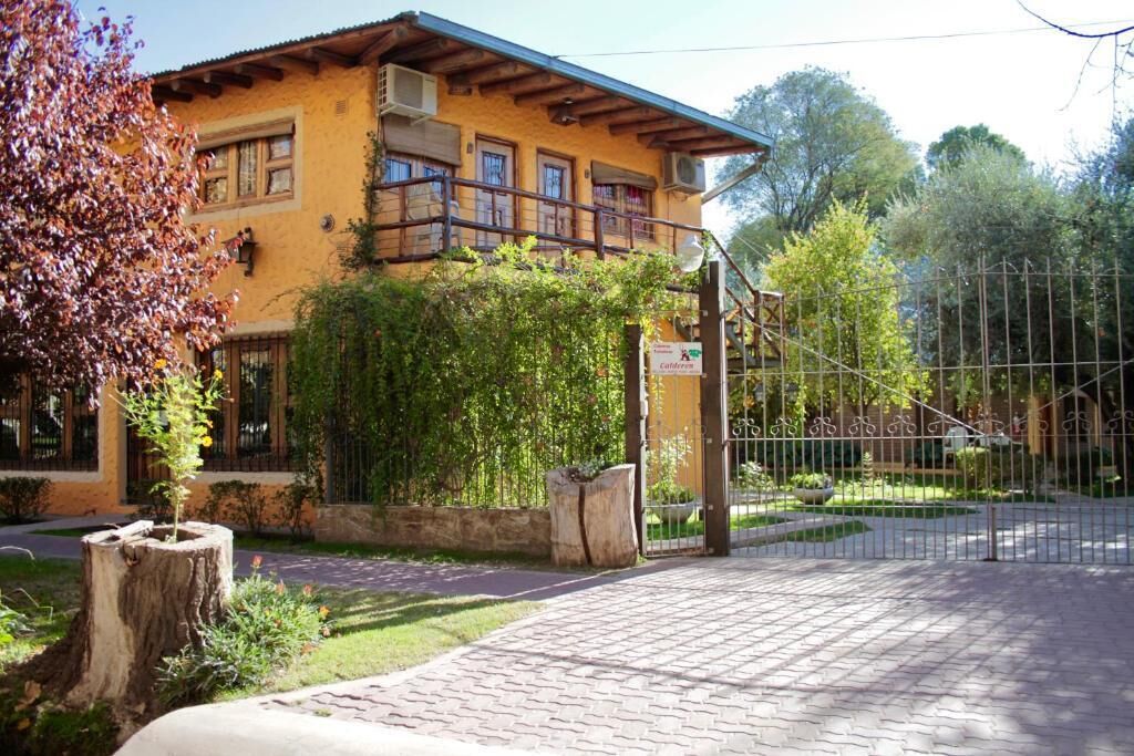 A yellow building with a balcony, a paved entrance, and a fenced garden area.