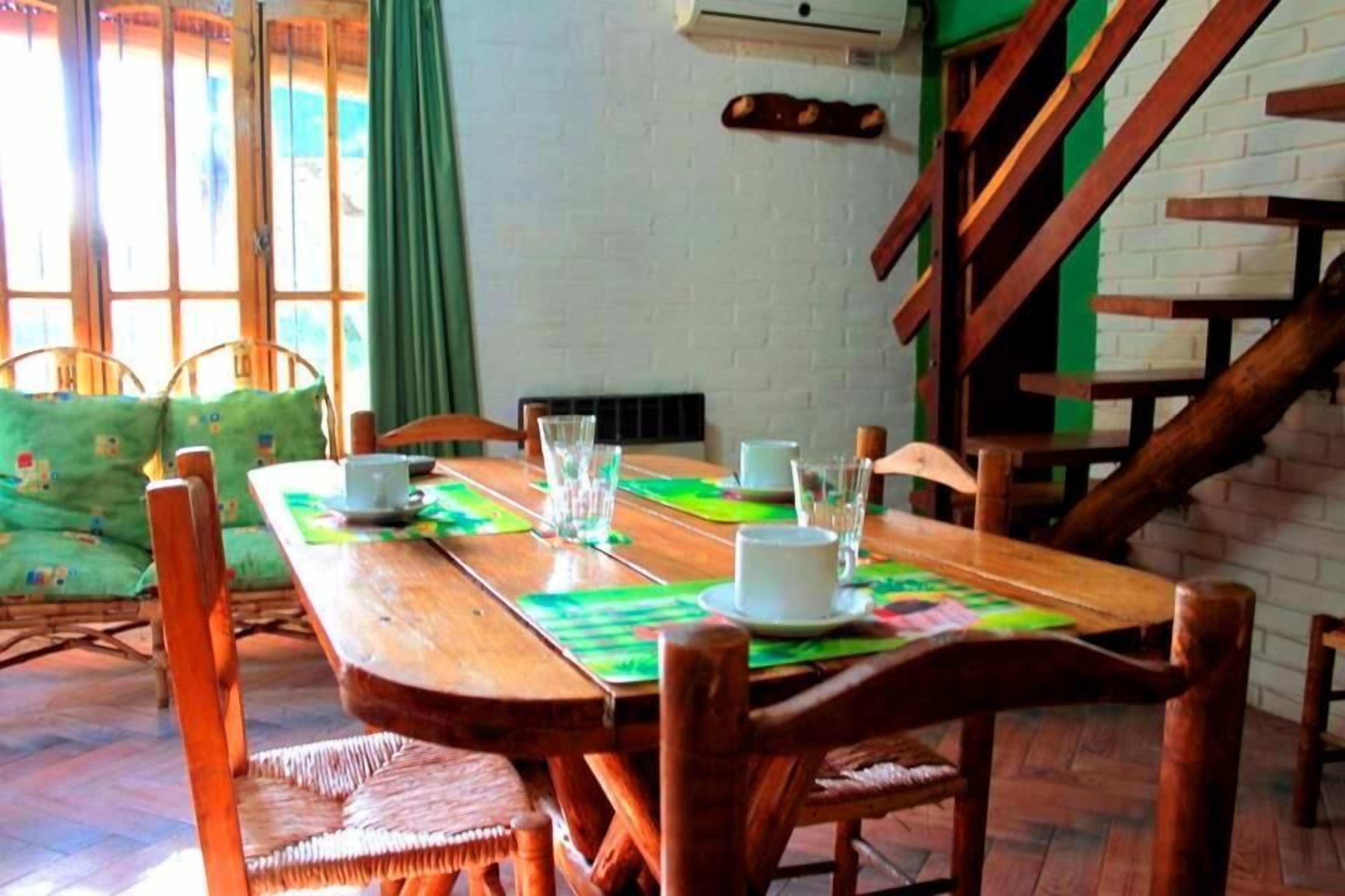 A wooden dining table with chairs, a green cushion, and a window with curtains.