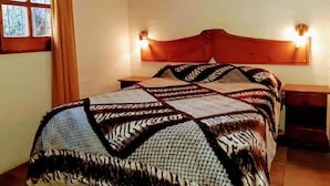 Un dormitorio con cama, cabecera con luces empotradas, ventana con cortinas y un cuadro en la pared.
