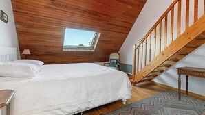 Ein Schlafzimmer mit Holzboden, einem Bett, einem Fenster und einer Holztreppe.