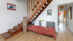 Eine Treppe mit Holzbalken und einem Geländer aus Holz, ein Sofa mit einer rot gemusterten Decke und einem gewebten Korb.