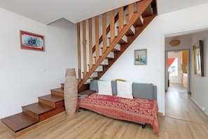 A staircase with wooden steps and a wooden railing, a sofa with a red patterned throw, and a woven basket.