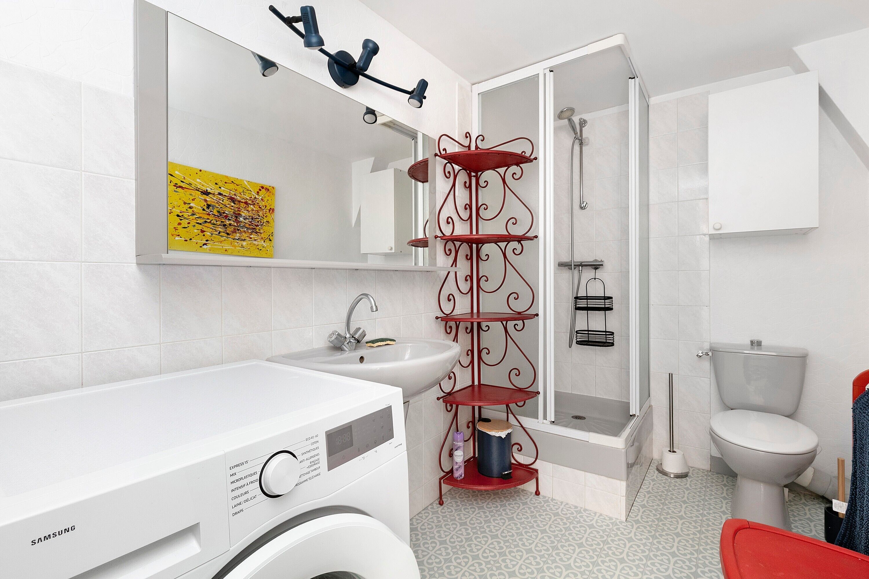Een moderne badkamer met een wit wastafelmeubel, een rode metalen plank, een toilet en een douche.